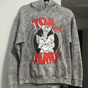 This medium gray hoodie features a playful Tom and Jerry design